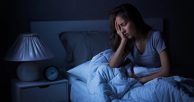 A young woman in bed at night, looking distressed | Trainest 