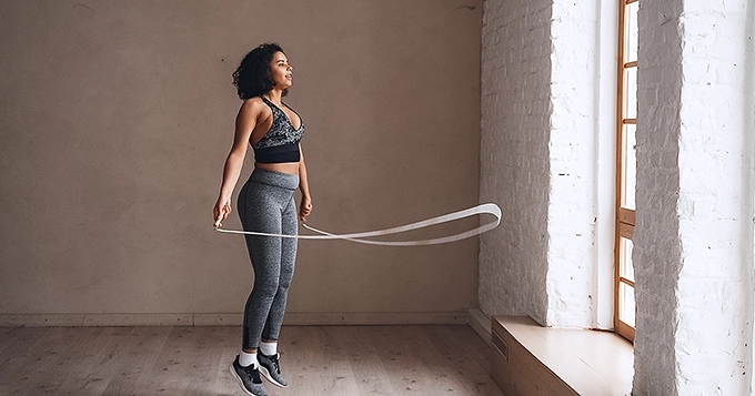 A woman exercising with a jumping rope indoors | Trainest
