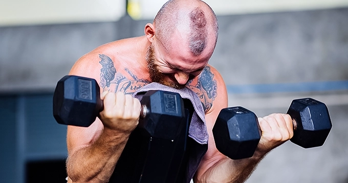 A rugged-looking man curling dumbbells | Trainest
