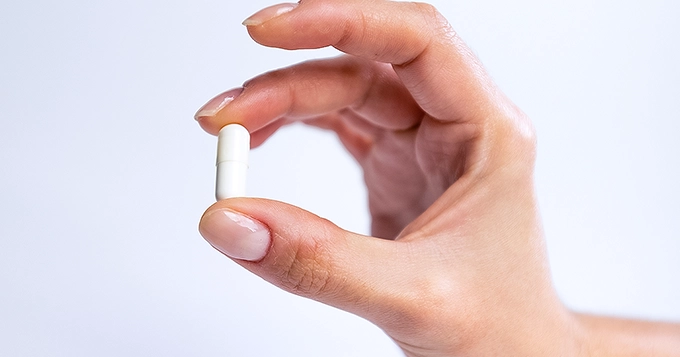 A close-up of a hand holding a vitamin capsule | Trainest 