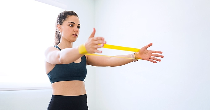 A woman exercising using a yellow looped resistance band | Trainest 