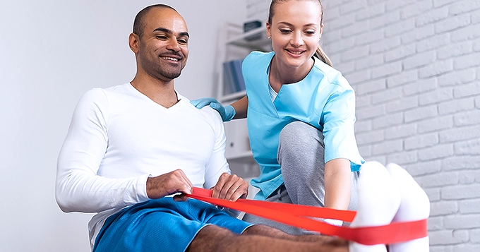 A man using a resistance band with the assistance of a physiotherapist | Trainest 