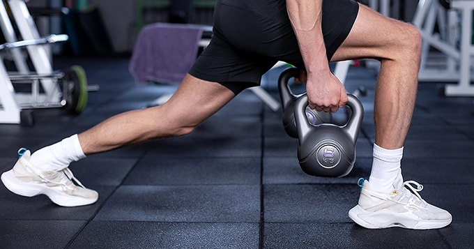 Someone doing kettlebell lunges in a gym | Trainest
