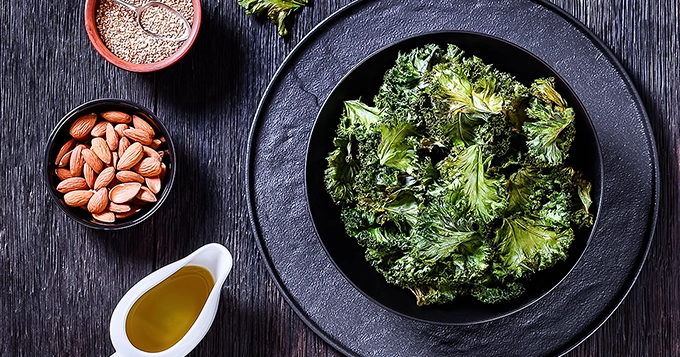 A plate of kale with small servings of nuts and seeds | Trainest 