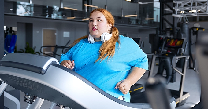 A heavyset woman running on a treadmill | Trainest
