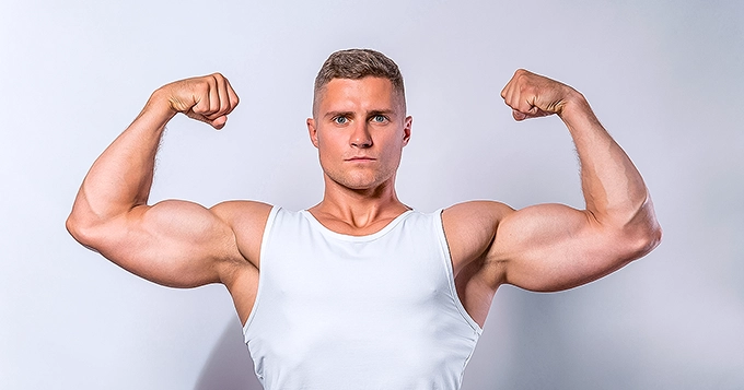 A muscular man flexing his arms in a front double biceps pose | Trainest 