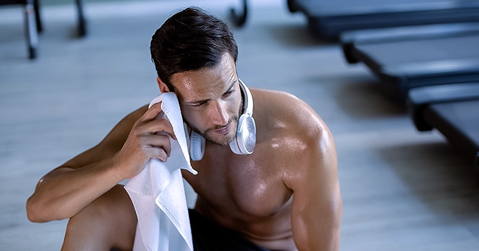 A fit, shirtless man sweating profusely inside a gym | Trainest 