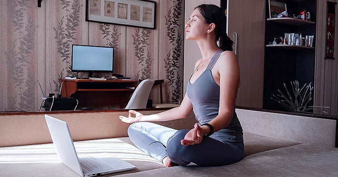 A woman doing Yoga with a laptop in front of her | Trainest 