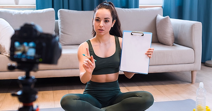 A Yoga instructor holding a clipboard while filming herself | Trainest 