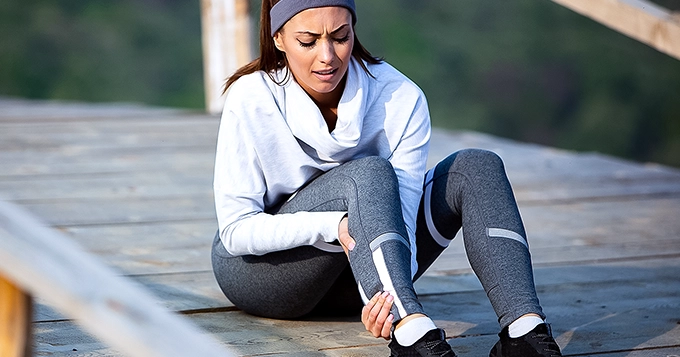 A woman in workout clothes suffering from muscle cramps | Trainest 