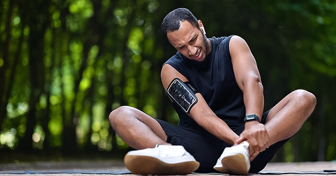 A man wincing in pain, holding his ankle | Trainest 