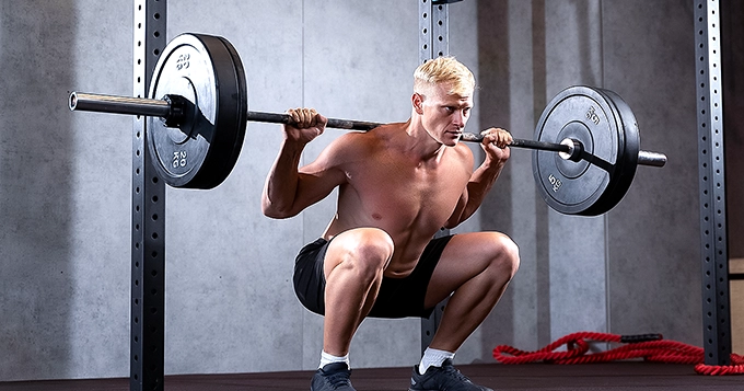 A fit man doing barbell back squats | Trainest
