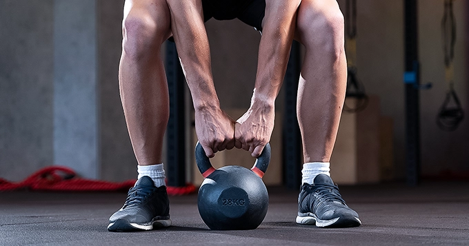 A fit person setting up to perform heavy kettlebell swings | Trainest
