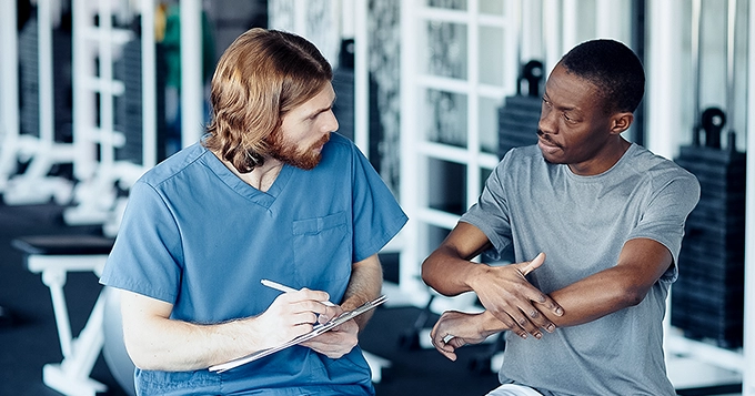 A physiotherapist talking to their client in a gym | Trainest
