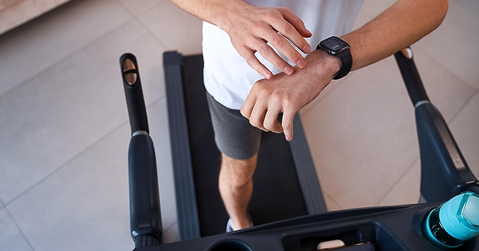 Someone walking on a treadmill while looking at their smartwatch | Trainest 