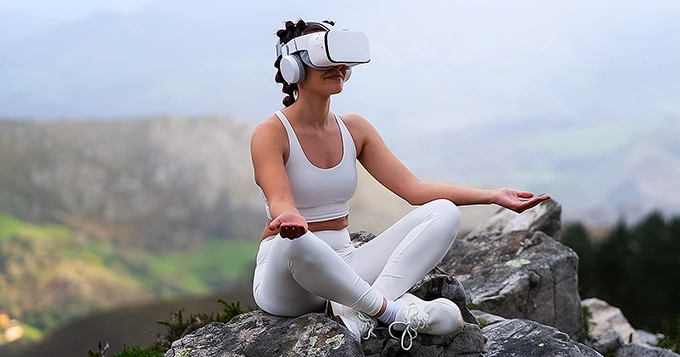 A woman meditating outdoors with a VR headset on | Trainest 