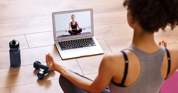 A woman following an online meditation class on her laptop | Trainest 