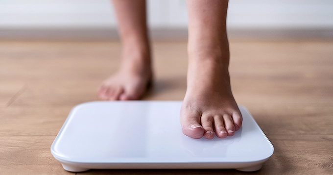 Someone stepping on a digital weighing scale | Trainest 