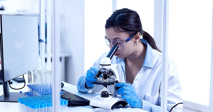 A biologist examining a specimen using a microscope | Trainest 