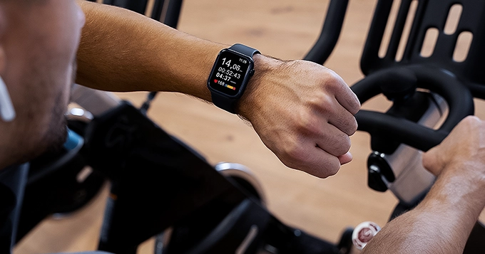 A man exercising on a spin bike while looking at his fitness tracker | Trainest 