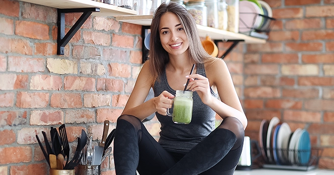 A woman in workout clothes drinking a smoothie | Trainest 