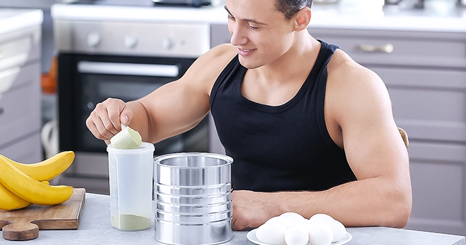 A fit man scooping in protein powder into a shaker cup | Trainest 