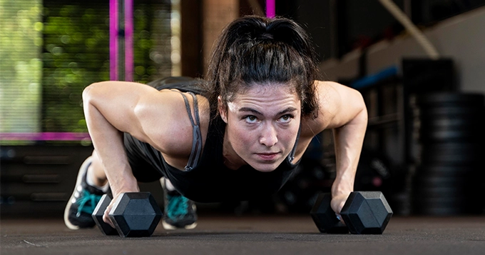 A woman performing a dumbbell push-up | Trainest 