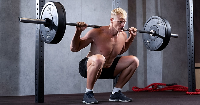 A man performing barbell back squats | Trainest
