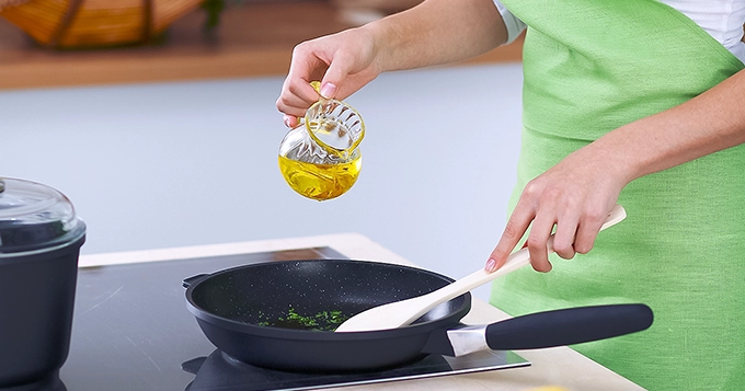 Someone pouring oil into a pan while cooking | Trainest 