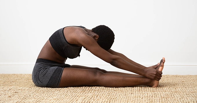 A woman on the floor doing a head-to-knee stretch | Trainest 