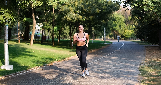 A woman in workout clothes jogging in a park | Trainest 