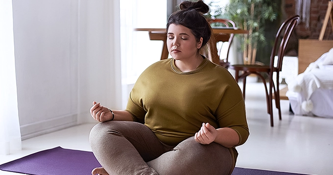 A heavyset woman meditating | Trainest 