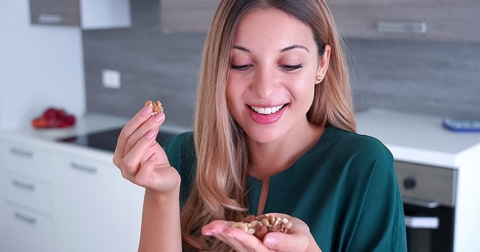 A woman snacking on a handful of nuts | Trainest
