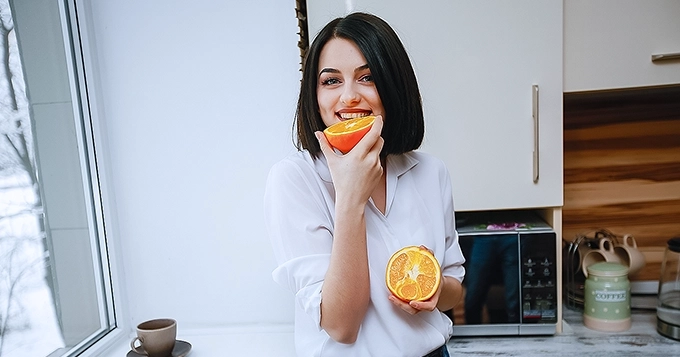 A woman eating an orange with a smile on her face | Trainest
