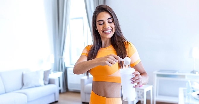 A fit woman scooping powdered supplement into her shaker cup | Trainest
