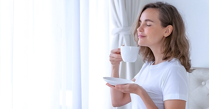 A woman enjoying a cup of coffee by the window | Trainest
