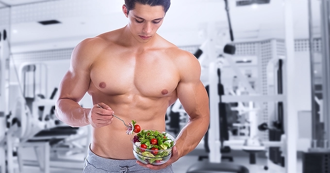 A muscular man eating a bowl of fresh salad | Trainest
