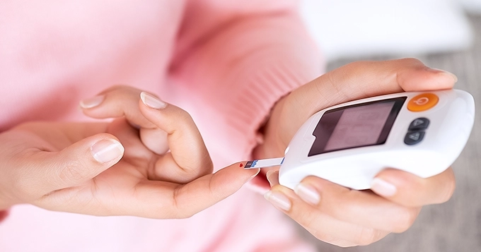 A close-up of a lady using a glucometer | Trainest
