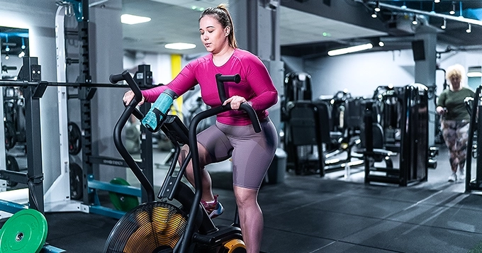 A heavyset woman working out on an air bike | Trainest
