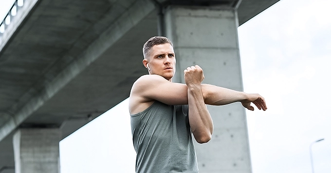 A man in workout clothes stretching his arms | Trainest
