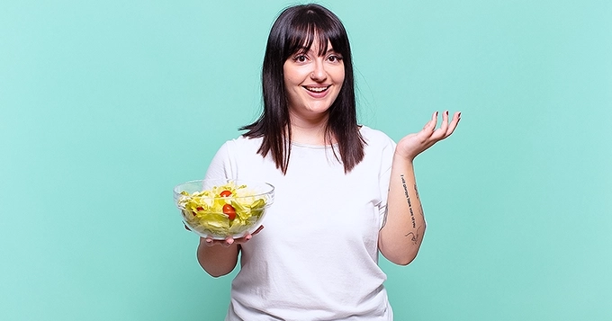 A slightly plump woman holding a salad bowl | Trainest
