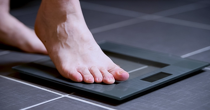 Someone getting his weight measurement on a digital weighing scale | Trainest
