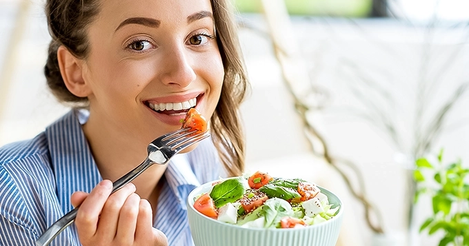 A woman eating a bowl of salad | Trainest
