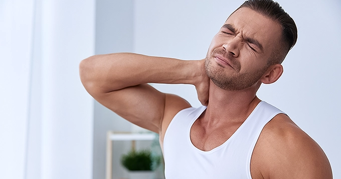 A fit man holding the back of his neck and grimacing | Trainest 