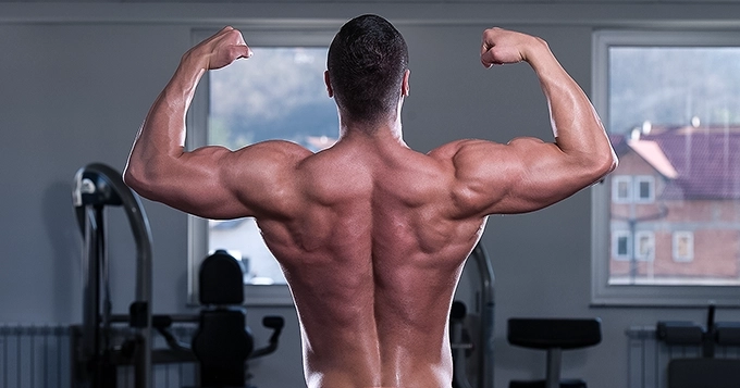 A muscular man flexing his back and arm muscles | Trainest 