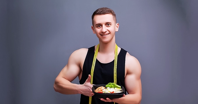 A fit man holding a healthy, meal-prepped chicken dish | Trainest 