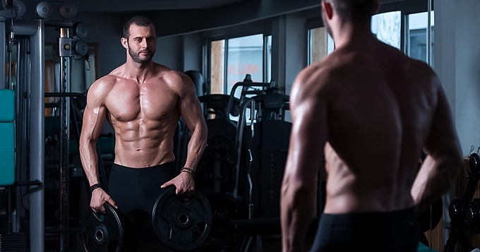 A muscular person looking at himself in the mirror while posing | Trainest 