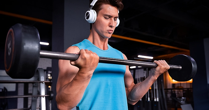 A fit guy in the gym listening to music while lifting weights | Trainest