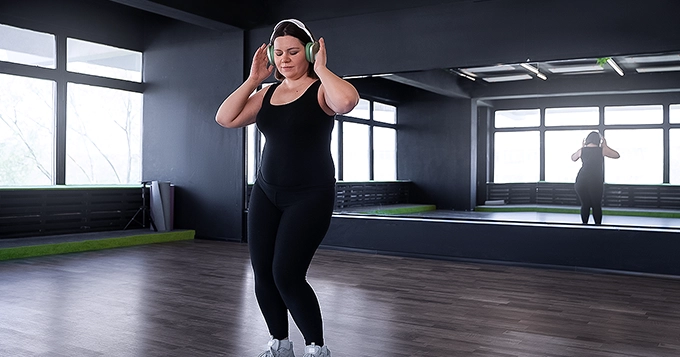 A lady dancing alone in the gym with headphones on | Trainest