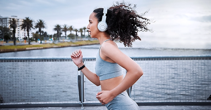 A fit woman running outdoors with headphones on | Trainest